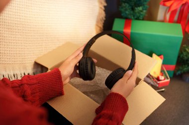 Noel hediyesi olarak heyecanlı bir şekilde kulaklıkları açan kişi, etrafı şenlikli süslemeler ve hediyelerle çevrili..