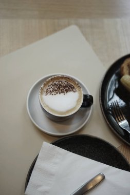 Ahşap masa üstü İskandinav usulü kapuçino kahvesi ile tatlının estetik bileşimini iç..