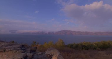 Ermenistan dağları arasında Sevan Gölü Panoraması. Bir köy yolu. Turistler geliyor. Keskin taşlar ve kayalar görülebilir. Bulutlar dağlara düşüyor. Turuncu çimenler sallanıyor