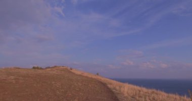 Ermenistan dağları arasında Sevan Gölü Panoraması. Bir köy yolu. Turistler geliyor. Keskin taşlar ve kayalar görülebilir. Bulutlar dağlara düşüyor. Turuncu çimenler sallanıyor