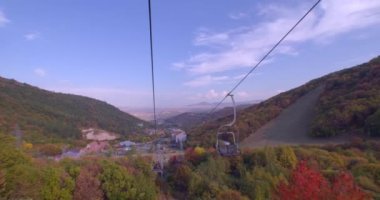 Ermenistan dağları arasında bir teleferik gezisi. Çöl kulübesi buradan geçiyor. Yeşil ve kırmızı ağaçlar yüzüyor. Sonbahar. Uzak dağlara ve şehre. Mavi gökyüzü. Bulutlar süzülüyor