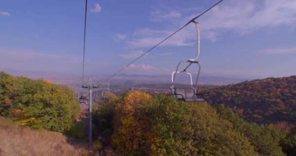 アルメニアの山の間でケーブルカーに乗る 砂漠の小屋が通りかかった 緑と赤の木々が浮かんでいます 遠くの山々と都市に 青い空だ 雲が浮かんでいる — ストック動画