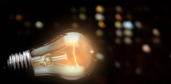stock image close up of tungsten light bulb with glow on dark background and night city lights