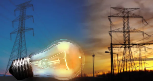 close up of tungsten light bulb with glow on background of high voltage electricity power lines