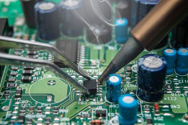 Atölyede bir teknisyenin ellerine yakın çekim. Tamirci bir IC lehimliyor SOIC paketinde bir elektronik cihazın devre kartına.