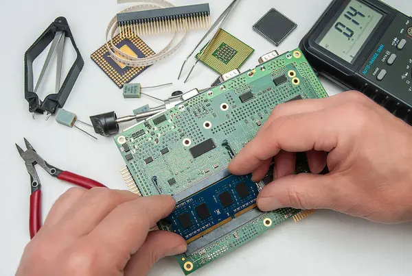 Close-up of a technician's hands in a workshop. The technician is installing a SODIMM memory module on an industrial embedded CPU board.