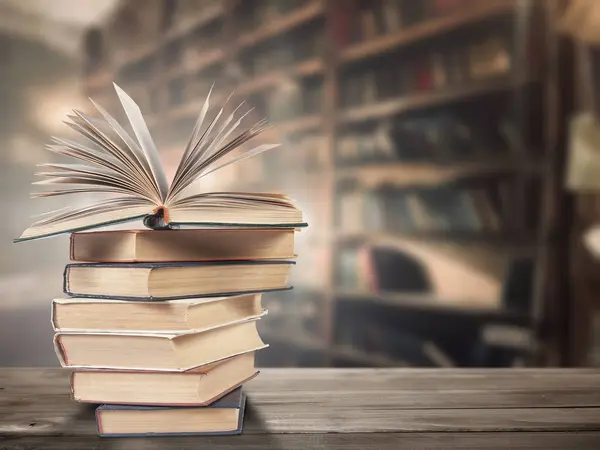 Kitap raflarının arka planına karşı ahşap bir yüzey üzerinde bir yığın eski kitap