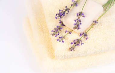 Üstünde lavanta çiçekleri ve beyaz sabun olan bir yığın yumuşak beyaz havlu, spa benzeri bir atmosfer yaratıyor..