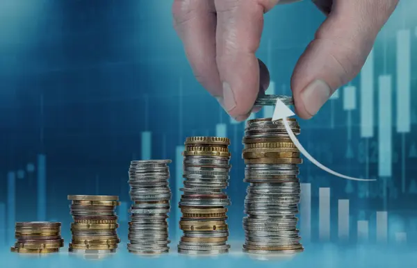 Finansal grafiklerin arka planına karşı el istifleme paraları, büyüme, yatırım ve finans kavramlarını sembolize eder.