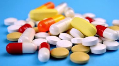 Açık mavi bir yüzey üzerinde kırmızı, beyaz ve sarı ile çeşitli ilaç haplarının yakın çekimi, sağlık ve tıbbı temsil eder..