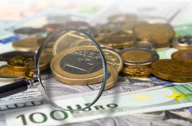 Büyüteç altında çeşitli uluslararası para birimleri ve sikkelerin ayrıntılı görünümü, mali analizi ve küresel ekonomi kavramlarını sembolize etmektedir..