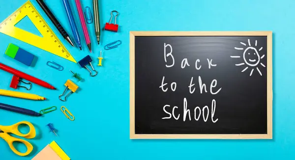 Renkli kırtasiye öğeleri ifadeyi gösteren bir yazı tahtasının etrafını sarar, okula geri döner, parlak mavi bir arkaplan karşısında ayarlanır.