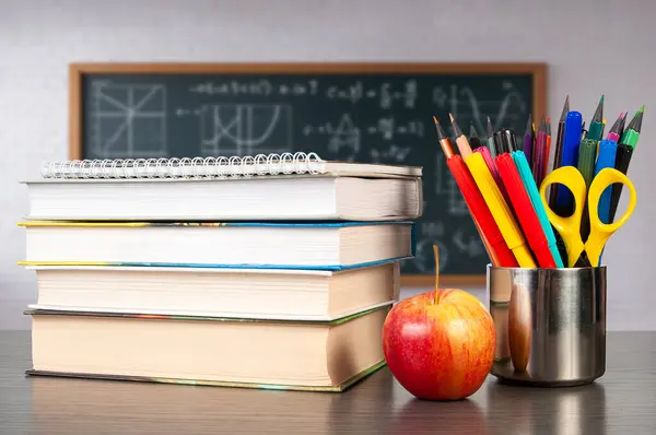 Bir yığın ders kitabı parlak kırmızı bir elma ve renkli kırtasiye ile dolu bir konteynırın yanında, bir sınıf çalışma oturumu için idealdir..