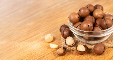 Tahta bir masada cam bir kasede sergilenen taze Macadamia fındıkları, vurgu için kasenin etrafına birkaç fındık konmuş..