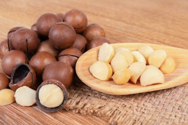 Kabuklu ve kabuksuz Macadamia fındıkları ahşap bir yüzeye yerleştirilmiş, kremsi iç ve karanlık dış kabuklarını sergiliyorlar..