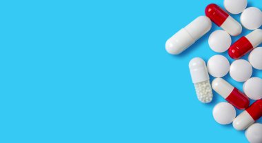 Kapsüllerin ve tabletlerin farklı şekilleri ve renkleri katı mavi bir arkaplana yayılarak, bunların sağlıktaki çeşitliliği ve önemini vurgulamaktadır..