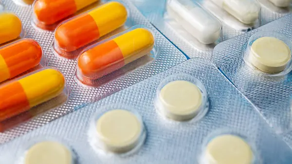 Farklı kapsüller ve tabletler özenle düzenlenerek gri bir arkaplanda farklı şekiller, boyutlar ve renkler gösterilir..