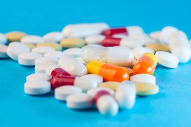 Değişik tiplerdeki hap ve kapsüller canlı mavi bir arka plana saçılmış, değişik şekilleri ve renkleri vurguluyorlar..