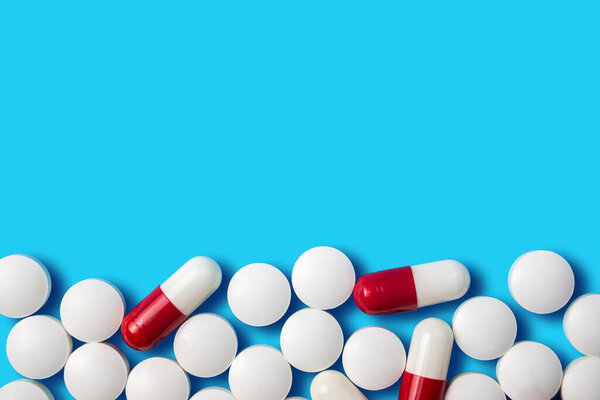 Different shapes and colors of capsules and tablets are spread across a solid blue background, highlighting their variety and significance in health.