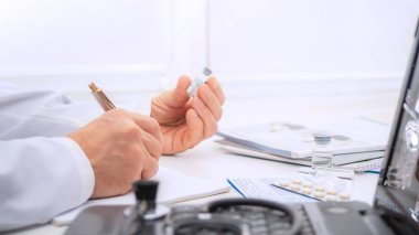 A healthcare worker is focused on organizing medications and documenting important information in a well-lit clinical workspace. clipart