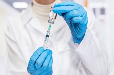 Yetenekli bir sağlık görevlisi, iyi aydınlatılmış bir klinikte aşı sıvısını şırıngaya boşaltıyor..