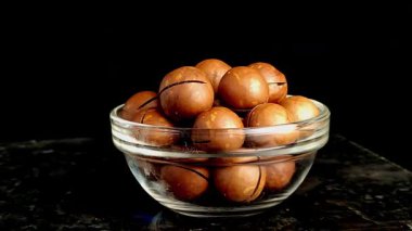 Koyu mermer bir arka planda cam kasede sergilenen taze Macadamia fındıkları..