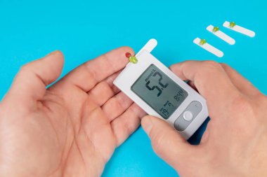 Kan şekeri ölçümlerini gösteren bir glukometre tutarken test bantları yakınlarda görünüyor. Bu da ev sağlığı yönetimini gösteriyor..
