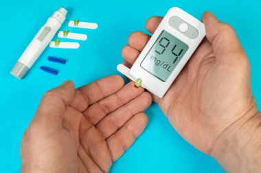 Kan şekeri ölçümlerini gösteren bir glukometre tutarken test bantları yakınlarda görünüyor. Bu da ev sağlığı yönetimini gösteriyor..