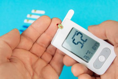 Kan şekeri ölçümlerini gösteren bir glukometre tutarken test bantları yakınlarda görünüyor. Bu da ev sağlığı yönetimini gösteriyor..