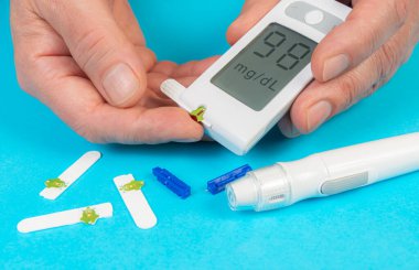 Kan şekeri ölçümlerini gösteren bir glukometre tutarken test bantları yakınlarda görünüyor. Bu da ev sağlığı yönetimini gösteriyor..