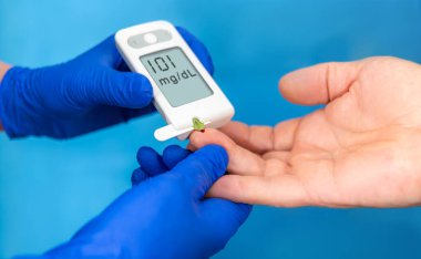 Bir sağlık uzmanı kan şekerini ölçmek için bir metre kullanır, klinik ortamda bir hastaya yardım eder, sağlık kontrolüne odaklanır..