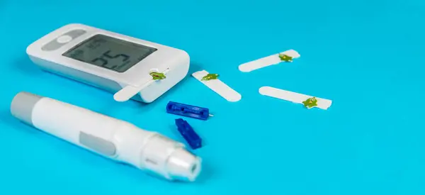 Kan şekeri ölçer ve insülin kalemini test şeritleri ve mızraklarıyla mavi bir arka plana yerleştirip diyabet yönetimi için yanlarına yerleştirmişler..