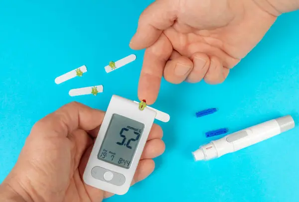 Kan şekeri ölçümlerini gösteren bir glukometre tutarken test bantları yakınlarda görünüyor. Bu da ev sağlığı yönetimini gösteriyor..