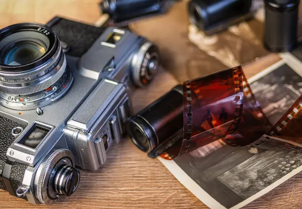 Klasik fotoğrafçılık nostaljisini çağrıştıran siyah ve beyaz fotoğraf ve film ruloları ile çevrili ahşap bir yüzeyde duran antika bir kamera..
