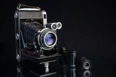 Değiştirilebilir lenslerle donatılmış, yansıtıcı siyah bir yüzey üzerinde zarif bir şekilde sergilenen, işçiliğini vurgulayan, ayrıntılı vintage kamera..