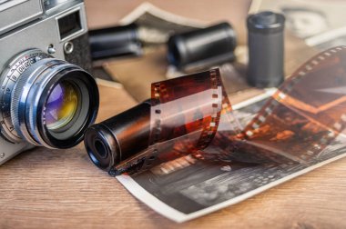 Klasik fotoğrafçılık nostaljisini çağrıştıran siyah ve beyaz fotoğraf ve film ruloları ile çevrili ahşap bir yüzeyde duran antika bir kamera..