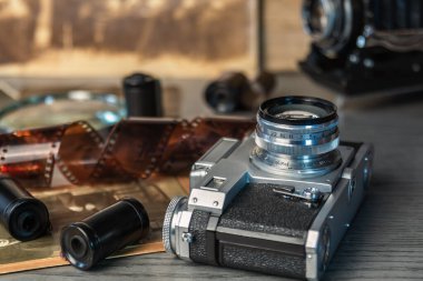 Klasik kamera, eski film makaraları ve fotoğraflarla çevrili ahşap bir masanın üzerinde duruyor. Nostaljik bir fotoğraf atmosferini çağrıştırıyor..