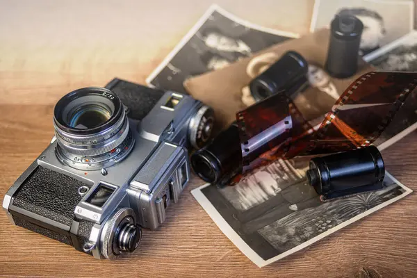 Klasik fotoğrafçılık nostaljisini çağrıştıran siyah ve beyaz fotoğraf ve film ruloları ile çevrili ahşap bir yüzeyde duran antika bir kamera..