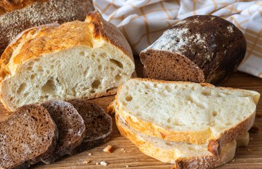 Tahta bir kesme tahtasına yerleştirilmiş farklı türde taze ekmek yakın bir yerde kumaş ve renkler sergileniyor..