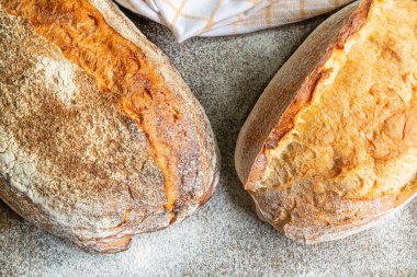 İki altın sarısı, kabuklu ekmek somunu dokulu bir tezgahın üzerinde, un ile hafifçe tozlanmış, sıcak bir fırın atmosferi sergiliyor..