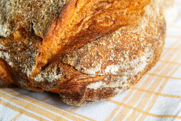 A round loaf of artisan bread, crusty and golden, sits on a linen cloth in a warm kitchen, inviting a cozy atmosphere.
