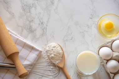 Un, yumurta, süt ve çırpıcı mermer tezgahın üzerine serilmiş sıcak bir mutfakta pişirme oturumuna hazırlanıyor..