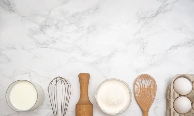 Bir mermer tezgah un, yumurta, süt, merdane, çırpıcı ve ahşap kaşık gibi pişirme gereksinimlerini gösterir..
