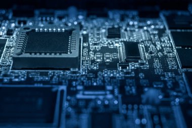 Karmaşık devre kartında çeşitli mikroçipler ve elektronik bileşenler var. Mavi ışıkta aydınlatılmış, ileri teknoloji sergileniyor..