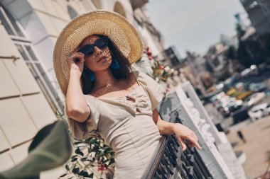 Zarif şapkalı güzel bir kadın balkonda dinlenirken gözlüklerini ayarlıyor.