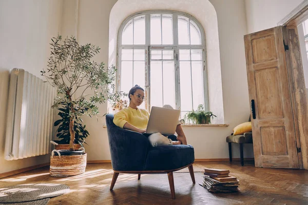 Evde Rahat Bir Sandalyede Otururken Dizüstü Bilgisayar Kullanan Güzel Bir — Stok fotoğraf