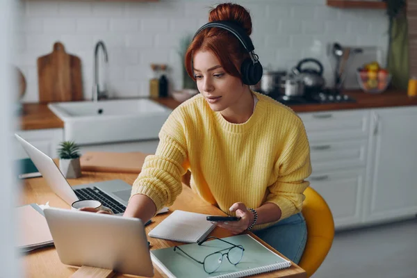 Stock image Beautiful woman in headphones using technologies while sitting at the kitchen counter