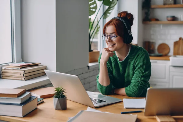 Όμορφη Νεαρή Γυναίκα Ακουστικά Κοιτάζοντας Laptop Και Χαμογελώντας Ενώ Εργάζονται — Φωτογραφία Αρχείου