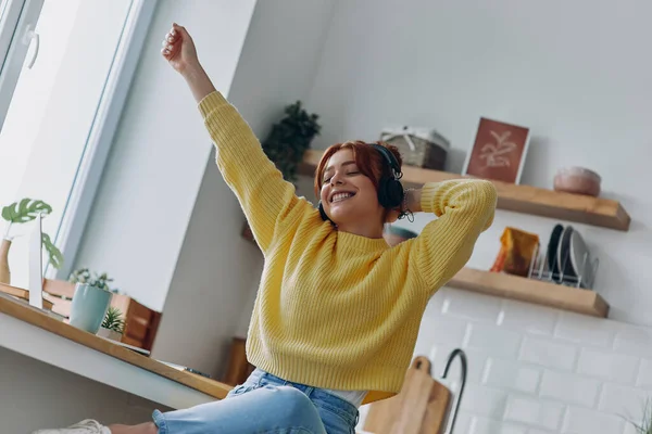 Радостная Молодая Женщина Наушниках Держит Руки Поднятыми Сидя Кухонным Столом — стоковое фото