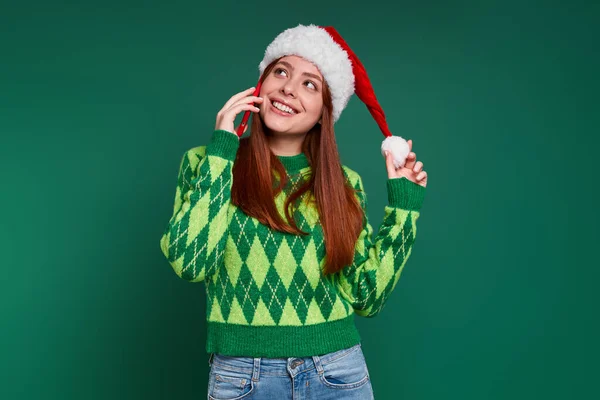 美しい若い女性ですクリスマスの帽子の話で携帯電話と笑顔で緑の背景 — ストック写真